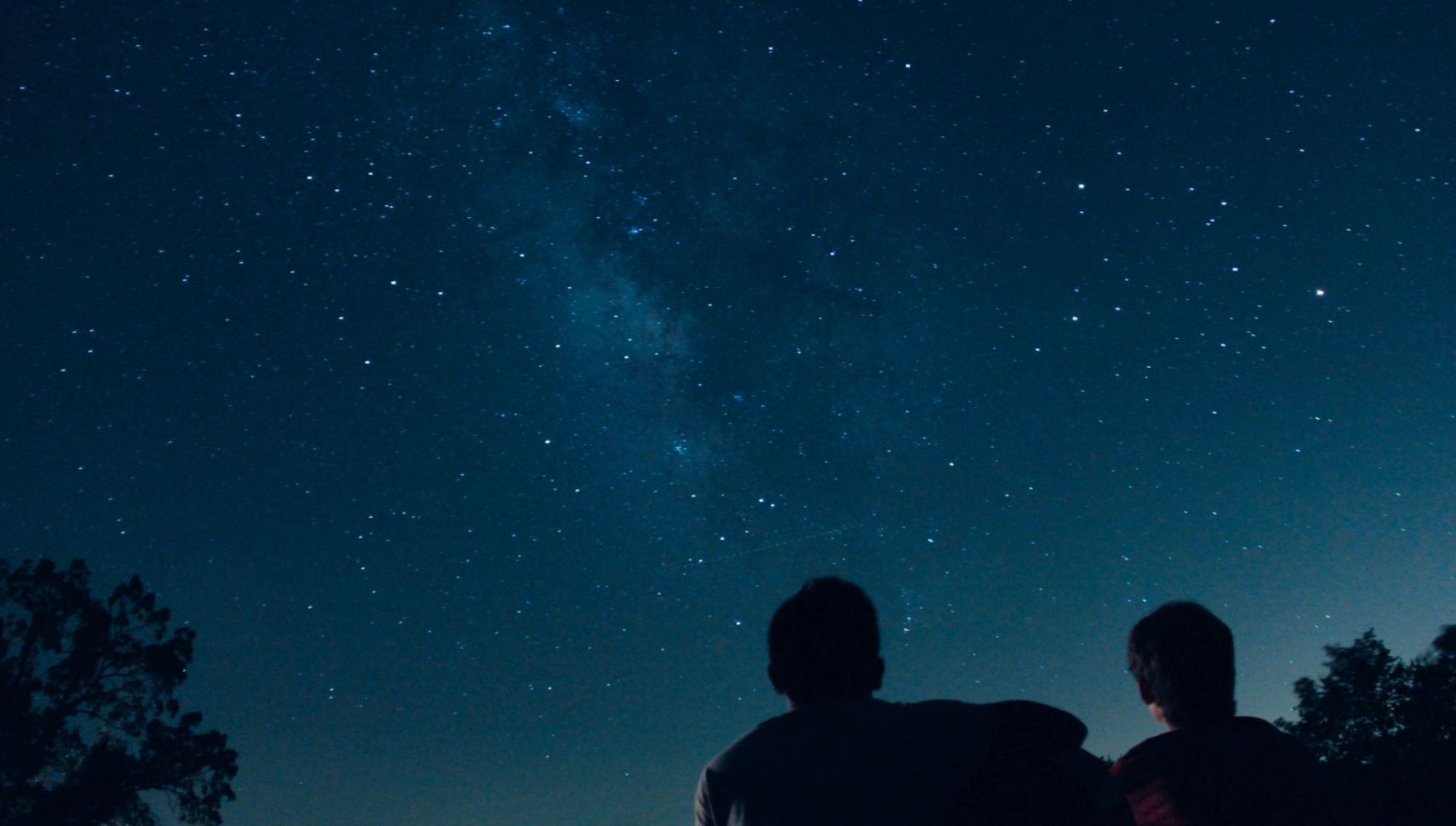 A Couple Of People Looking At The Sky With Stars In The Sky